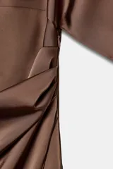 Vestido midi de satén color marrón, con cuello redondo, manga corta con capa fluida y cintura entallada con pliegues. Cuenta con falda recta con abertura en el bajo y cierre lateral con cremallera oculta.