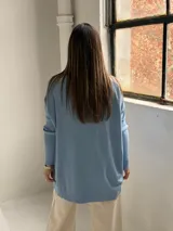 Sweater de punto color celeste, con cuello redondo, corte holgado y mangas largas con puños acanalados. Presenta un detalle de costura vertical central en el frente.