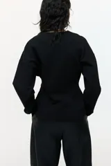 Blazer negro de punto grueso, corte entallado con hombros caídos, escote en V, cierre frontal de botones y bolsillos insertados decorativos.