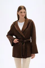 Chaqueta blanca de corte holgado con capucha, cierre frontal cruzado con botones y cinturón de tela ajustable. Presenta detalles de costuras decorativas en color negro en los bordes, solapas, bolsillos y cinturón.