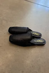 Mules negros con capellada de cuero y tejido calado, con suela plana y detalle de costuras en el borde.