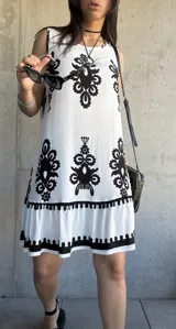 Vestido corto blanco con estampado de flores negras, corte suelto y ruedo con volantes.
