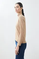 Remera de punto color tostado melange, con cuello alto con volados y mangas largas.