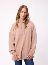 Canguro oversize de la marca Rusty, color beige, con capucha y cordones ajustables. Presenta un pequeño parche con el logo de la marca en el pecho y puños acanalados.