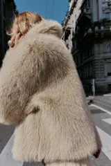 Cazadora de pelo sintético en color beige, con cuello solapa, manga larga y cierre frontal con cremallera. Presenta un diseño de corte recto y acabado suave.