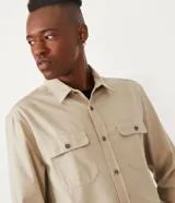 Camisa de corte regular, color beige, con cuello camisero, mangas largas, cierre frontal con botones y dos bolsillos con solapa en el pecho.