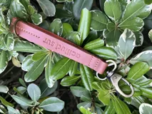 Llavero de cuero en formato de tira con diseño minimalista, confeccionado en cuero genuino marrón con interior en contraste color fucsia, pespuntes rosados y herrajes metálicos envejecidos con gancho tipo mosquetón.
