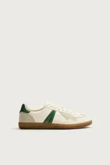 Zapatillas de estilo retro para hombre, color blanco off-white con detalles en verde oscuro y suela de goma marrón estilo gum. Presenta cordones al tono, refuerzos en gamuza en la puntera y talón, y bandas laterales verdes en contraste.