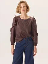 Camisa de color marrón con diseño combinado, presentando mangas abullonadas con volados en los hombros y cuerpo de algodón. Combina una textura de tela de camisa en mangas y delantero con una espalda de tejido elástico.