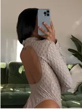 Body de manga larga y cuello alto, color tostado, con diseño de espalda descubierta y tejido texturado con patrón geométrico tridimensional.