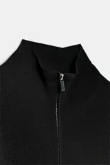 Chaqueta de punto negra con cuello subido y cierre frontal con cremallera, de manga larga y diseño ajustado.