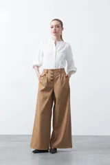 Camisa blanca de manga larga con silueta relajada, confeccionada en tejido fluido. Presenta cuello redondo con pequeña abertura, cierre frontal con botones y detalle de tablas en los hombros.