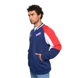 Campera deportiva Umbro del Club Nacional de Football, con cierre frontal, cuello y puños acanalados, y bolsillos laterales. Diseño en azul marino con mangas raglán en blanco y rojo, y escudo del club bordado en el pecho.