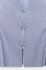Camisa de cuello subido y manga sisa, confeccionada en tejido a rayas azules y blancas. Presenta bajo acabado en peplum y cierre frontal con nudos de pasamanería.