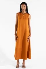 Vestido largo sin mangas de color mostaza, de corte recto y holgado, con escote redondo y bolsillos laterales. Confeccionado en mezcla de lyocell, viscosa y lino.
