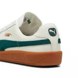 Championes Puma modelo Army Trainer, de diseño retro en color blanco con detalles en verde oscuro y suela de goma color caramelo. Presenta refuerzos de gamuza en la puntera y el logo de la marca en dorado en el lateral.