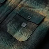 Camisa de manga larga confeccionada en mezcla de lana y poliéster con diseño de cuadros degradados en tonos verdes y marrones. Presenta cierre frontal con botones a presión, dos bolsillos frontales con solapa y paneles reforzados en los codos.