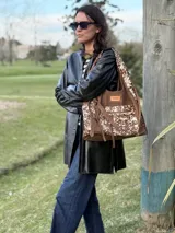 Cartera tipo shopper confeccionada en cuero marrón y detalles en pelo con estampado animal print tipo vaca, con bolsillos exteriores y tiras colgantes decorativas.