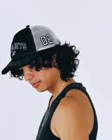 Gorro estilo trucker de color negro con paneles traseros de malla blanca. Presenta bordado frontal con el texto "TWOJEYS" en blanco y dos estrellas contorneadas debajo. El borde de la visera tiene costuras blancas y un acabado desgastado/roto.