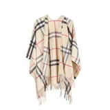 Poncho de tejido de punto con diseño de cuadros escoceses en tonos beige, negro y rojo. Presenta un corte amplio, cuello abierto y terminaciones con flecos en el ruedo.
