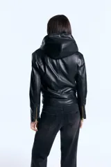 Campera de cuero ovino con capucha amplia integrada, cruce asimétrico con cierre metálico y cinturón regulable en la cintura. Presenta mangas largas con cierres metálicos en los puños y diseño estructurado.