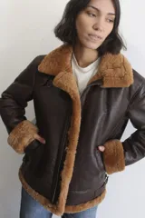 Campera bomber de cuero genuino color marrón oscuro, con interior y detalles en piel sintética color crema. Presenta cierre frontal, cuello solapa amplio y correas ajustables en el cuello y la cintura.