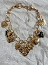 Collar dorado con cadena gruesa de eslabones y cadena fina de bolitas. Incluye varios dijes de corazones dorados con diferentes texturas y diseños, algunos con detalles en esmalte negro.