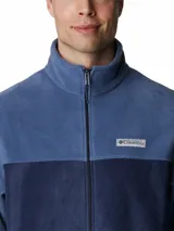 Campera polar Columbia con cierre frontal completo, cuello alto y bolsillos laterales con cierre. Presenta un diseño de bloques de color en dos tonos de azul y el logo de la marca bordado en el pecho.