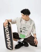 Remera de manga corta color nude con efecto tie-dye o goteo en tonos grises y blancos. Presenta un estampado gráfico frontal con tipografía estilo metal/rock, el texto "RETROGRADES", y el número "06" en verde menta.