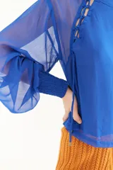 Blusa azul de crepe con transparencias y mangas largas abullonadas. Presenta detalle de lazos en los hombros y laterales.