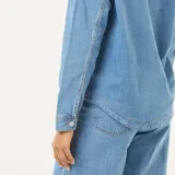 Camisa de jean de manga larga en tono azul medio, con cuello camisero, escote en V profundo y un bolsillo aplicado en el pecho.