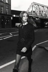 Blazer de cuello redondo y manga larga, confeccionado en tejido de tweed con textura. Presenta un diseño entallado con cinturón forrado a tono con hebilla metálica y cierre frontal mediante botones a presión ocultos.