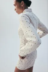 Chaqueta entallada de cuello redondo y manga larga, con cierre frontal de cremallera y falsos bolsillos de solapa en el delantero. Presenta un diseño estampado de lunares.