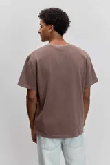 Remera de algodón color marrón con efecto lavado, de corte clásico y cuello redondo. Presenta un pequeño bordado de un pájaro en el pecho.