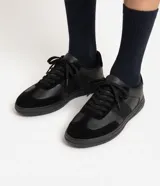 Championes urbanos para hombre en color negro, con diseño monocromático de perfil bajo. Combinan inserciones de material sintético y textura tipo gamuza en la puntera y laterales, con cierre de cordones al tono.