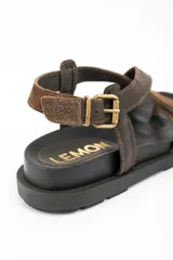 Sandalias de cuero marrón con tiras cruzadas en el empeine, suela chunky negra y hebilla metálica de ajuste en el talón.