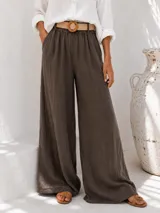 Pantalón palazzo marrón de corte ancho, con cintura elástica fruncida y bolsillos laterales. Incluye pascintos y un cinturón de rafia trenzada con hebilla redonda.