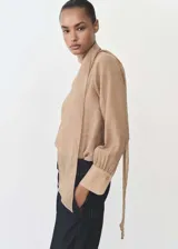 Blusa color beige con textura, cuello alto con lazo, mangas largas con puños abotonados y corte recto.