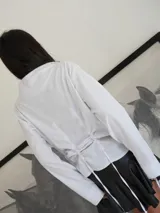 Camisa de lino color azul marino, con cuello alto, cierre frontal de botones y diseño ajustable mediante cordones en la parte inferior que permiten fruncir la prenda.