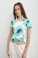 Remera de manga corta con estampado estilo acuarela en tonos de turquesa, verde y blanco, de cuello redondo y corte ajustado.