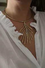 Gargantilla rígida dorada con dije colgante en forma de rama de árbol, con detalles plateados. El dije se puede usar con otras gargantillas.