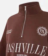 Buzo de algodón y poliéster color marrón, con cuello alto y cierre frontal parcial. Presenta diseño de hombros caídos, puños y ruedo acanalados, y estampado tipográfico frontal con la palabra Nashville.