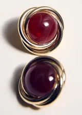 Pendientes circulares con aro dorado entrelazado y una piedra de resina color burdeos en el centro.