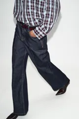 Jeans de tiro alto color azul oscuro, con cinco bolsillos, pernera ancha y nervio marcado en el delantero. Incluye un cinturón fino de cuero sintético marrón con textura de cocodrilo. Cierre frontal con cremallera y botón.