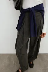 Pantalón balloon de tiro alto y diseño abuchonado, en color marrón oscuro con sutiles rayas verticales. Cuenta con pinzas y pliegues pronunciados en el delantero.