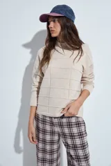Sweater de punto gris con cuello a la base y diseño de trama geométrica en relieve. Presenta un calce relajado con mangas largas y puños tejidos.