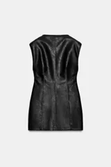 Vestido corto de cuero sintético negro con cuello redondo, manga sisa, hombreras y costuras marcadas que aportan estructura. Presenta bajo con volumen y cierre en la espalda con cremallera metálica.