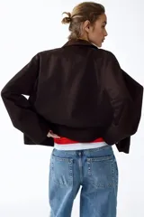 Campera de sarga color marrón oscuro, con cuello camisero de pana, cierre frontal oculto por solapa con botones a presión y bolsillos frontales grandes con solapa.