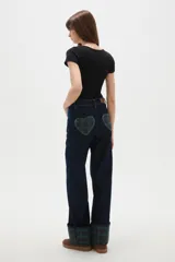 Pantalón de jean azul oscuro de corte recto y tiro alto, con costuras en contraste y dobladillo con vuelta que revela un estampado de cuadros en tonos verdes y azules.