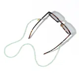 Correa para lentes Meller modelo Yaro, compuesta por cuentas de cristal semitransparentes en color verde. Incluye enganches metálicos dorados ajustables para gafas y una chapa de acero inoxidable con el logo de la marca grabado.